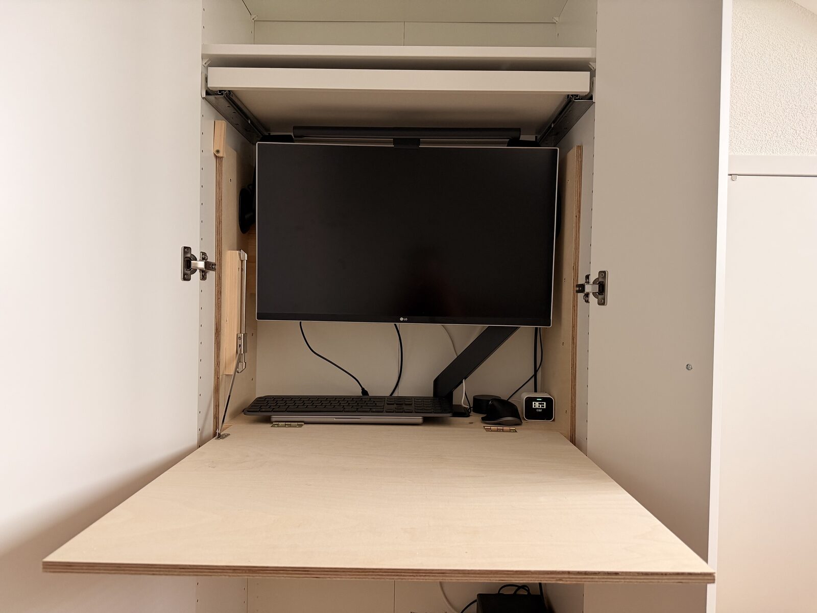 Monitor on a VESA arm above the folded-down plywood desk surface